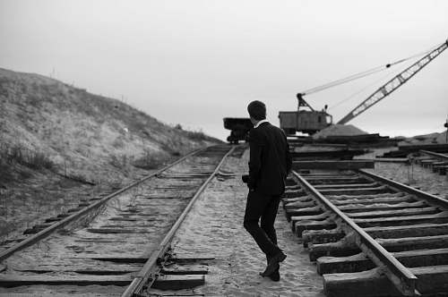 person grayscale of man walking on train rail black-and-white