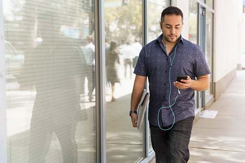 person man in blue button-down shirt walking beside glass wall during dayhtime people