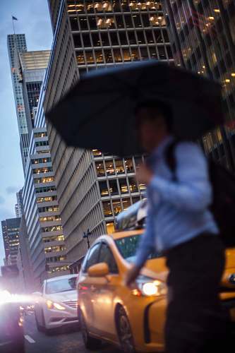 person man in blue dress shirt holding umbrella crossing street during daytime people