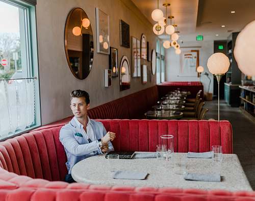 person man sitting on red fabric sofa near glass window restaurant
