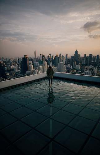person man standing on top of building facing high-rise building under gray sky urban