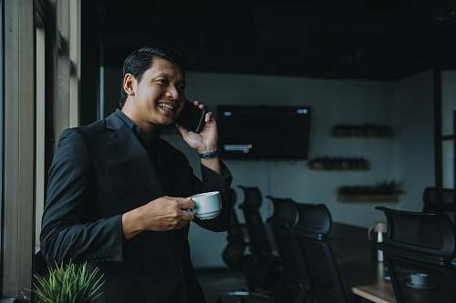 person smiling man holding cup and using smartphone coat