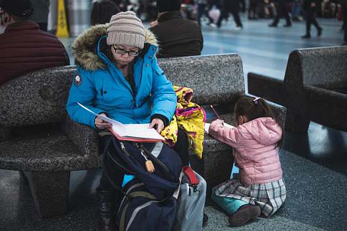 apparel woman sitting beside girl writing on bench clothing
