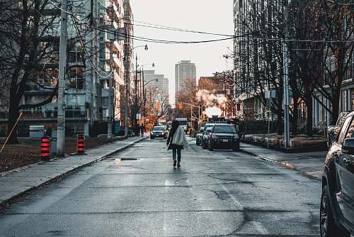 city woman walking near vehicles parked on road between large buildings road