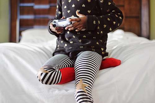 games children holding gray game controller sitting on white bed children