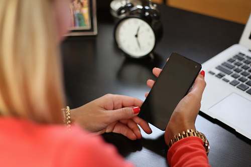 clock woman sitting holding smartphone near laptop phone