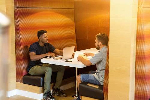 human man sitting on black leather bench holding gray laptop computer on top of white wooden table person