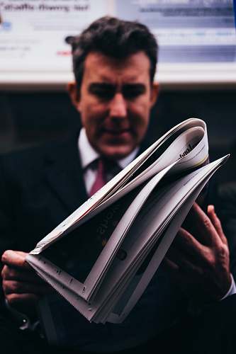 human selective focus photo of man in suit holding newspaper person