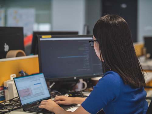 person woman using black laptop computer near turned on flat screen computer monitor human