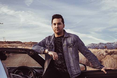 human closeup photo of man wearing gray denim jacket leaning on car car