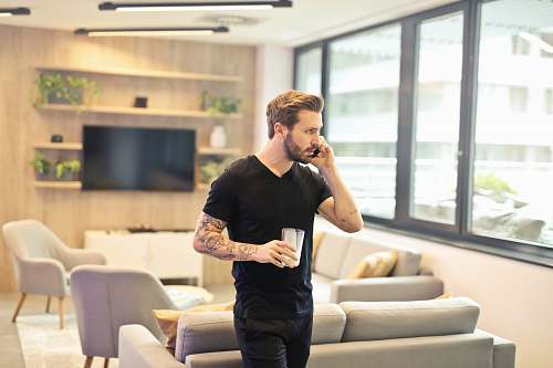 human man holding drinking glass while taking a call on phone couch