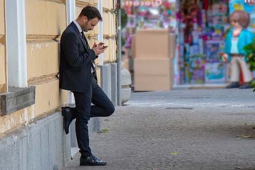 human man holding his phone while leaning on building people