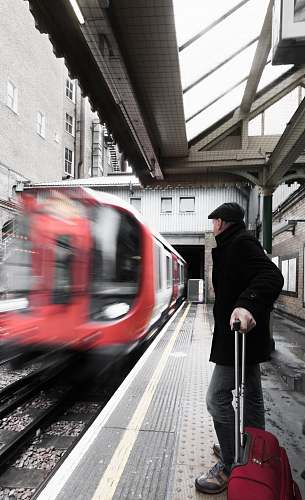 train man holding luggage waiting on railway with red train passing by people