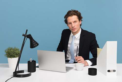human man sitting on chair beside laptop computer and teacup sitting