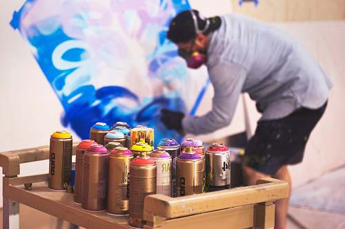 human paint sprays on table in front man painting on wall people