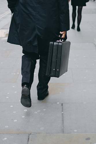 human person carrying suit case while walking on pavement people