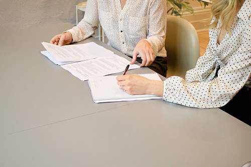 human woman signing on white printer paper beside woman about to touch the documents sitting