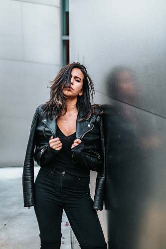 human woman touching her black leather jacket while standing near silver wall people