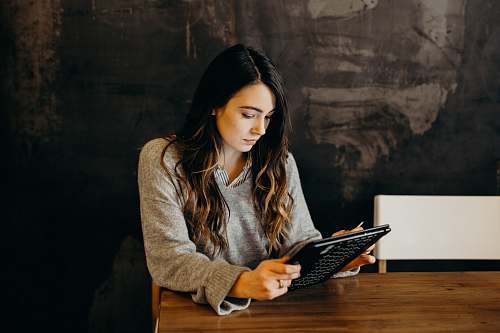 human woman wearing white dress shirt using holding black leather case on brown wooden table wood