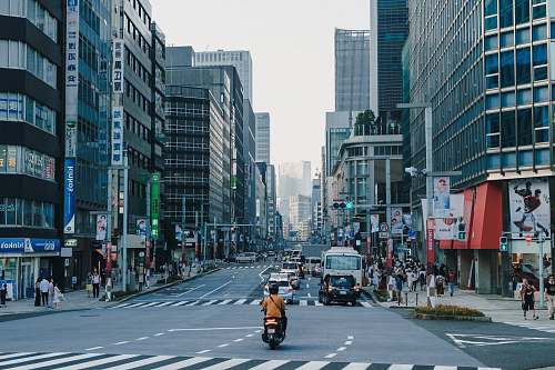 asphalt people and cars on road near buildings tarmac