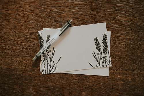 paper white pen on top of two white and black floral stationeries pen