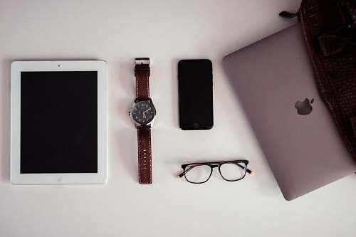 accessory white iPad beside round silver-colored analog watch, black iPhone 5 and black framed eyeglasses on white surface accessories
