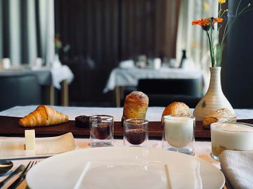 food four baked breads on brown wooden table beside shot glasses croissant