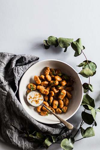 bowl bowl of nuts with spoon beside green leaves vegetable