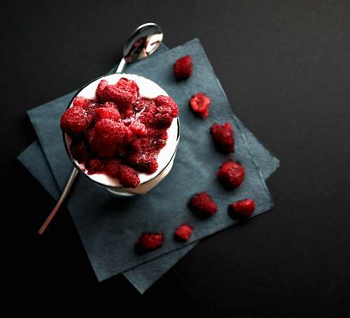 dessert bowl of red strawberries beside silver spoon raspberry
