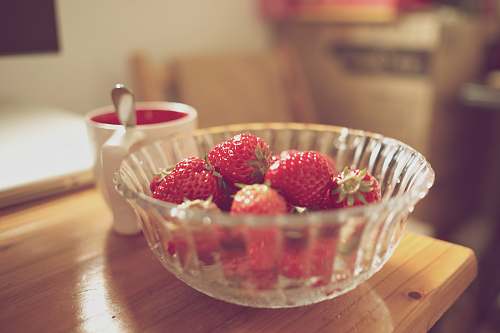 fruit bowl of strawberries beside white mug on table plant