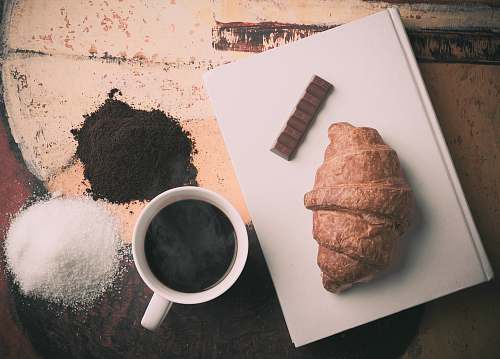 croissant bread on white book beside ceramic mug bread
