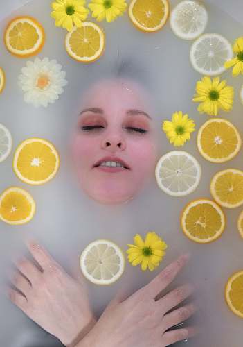 plant flat-lay photography of woman dipped in water surrounded by yellow lemons and flowers citrus fruit