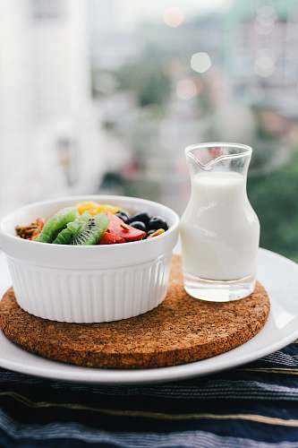 healthy fruit salad inside bowl beside glass of milk on brown board bowl