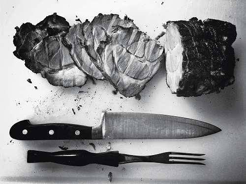 black-and-white grayscale photo of grilled meat beside knife and fork grey