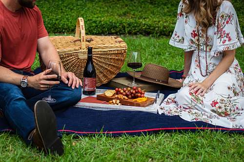 meal man and woman sitting on blue textile beside brown wicker picnic basket vacation