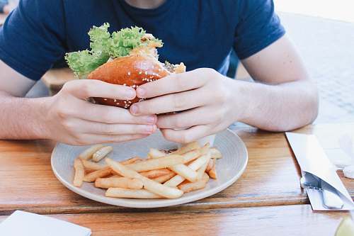 human person eating hamburger with fries on plate fries