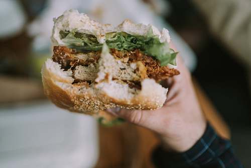 burger person holding hamburger with patty and vegetable fillings bite