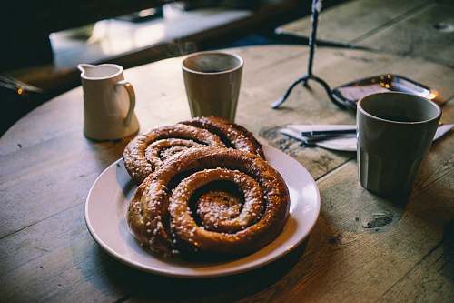 cup plate of glazed bread near mugs on tabletop breakfast