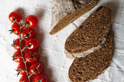 bread red cherry tomatoes beside sliced bread on white textile plant