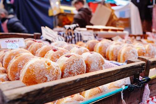 person selective focus photography of doughnuts display on brown wooden trays near person wearing black hoodie donut