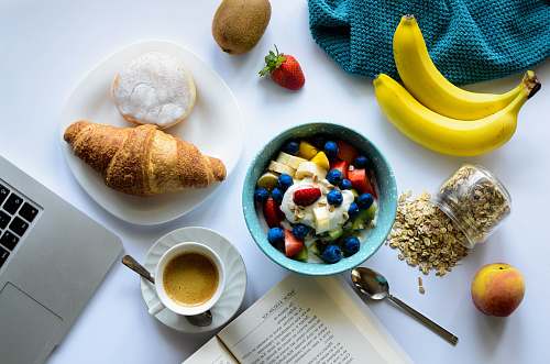 breakfast top view of strawberry and berries parfait in bowl near croissant and laptop meal