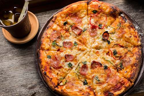 bowl top view photo of pepperoni pizza beside brown cup filled with yellow liquid and ice cubes pizza