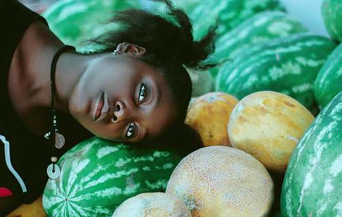 plant woman wearing black and white shirt leaning head on green watermelon fruits near cantaloupe melon