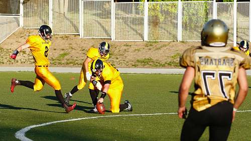 human football player about to kick a football held by another player during daytime person