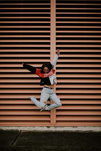 clothing woman jumping in front of brown wall people