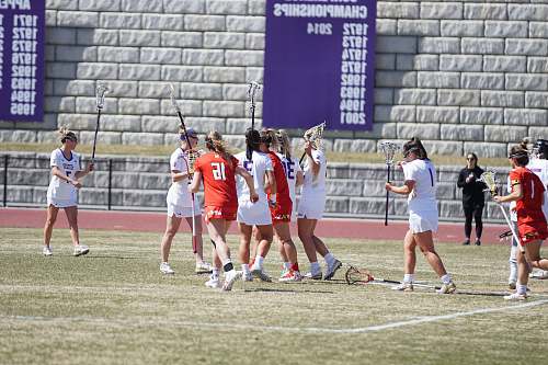 human women in red and white team jerseys playing lacrosse person