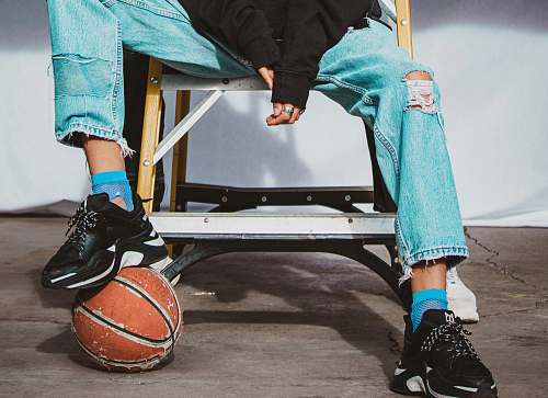 apparel person sitting on chair while stepping on orange basketball shoe