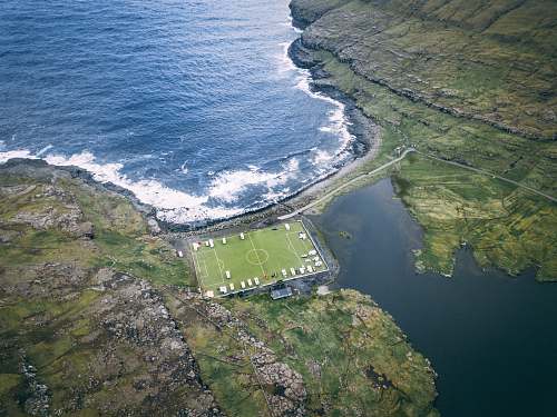 field aerial photo of soccer field near body of water during daytime team sport