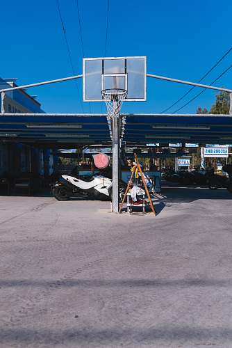 people basketball system in front of white sports bike parked under blue roofed space during daytime person