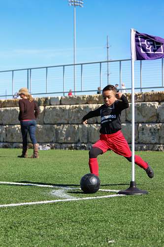 person boy about to kick soccer ball on green field under blue and white sky during daytime soccer